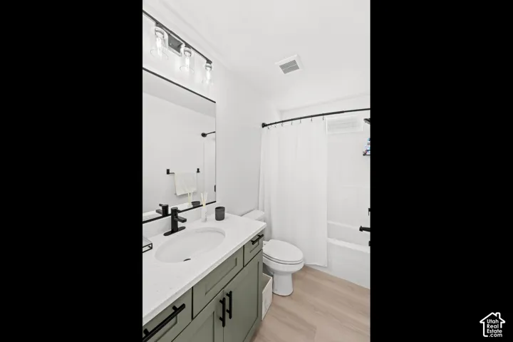 Contemporary bathroom featuring a sage green vanity with matte black hardware, a white countertop with an integrated sink, and wood-finish flooring