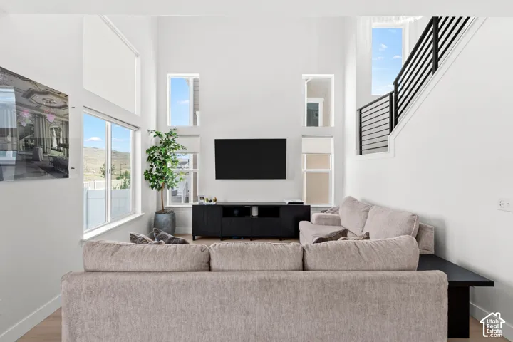 Double-height ceiling, large windows with mountain scenery, sleek black metal staircase railing, light wood-finish flooring, and a built-in media console