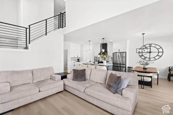 Open-concept living area featuring high ceilings, wood-finish flooring, a modern staircase with black metal railings, and a kitchen with stainless steel appliances
