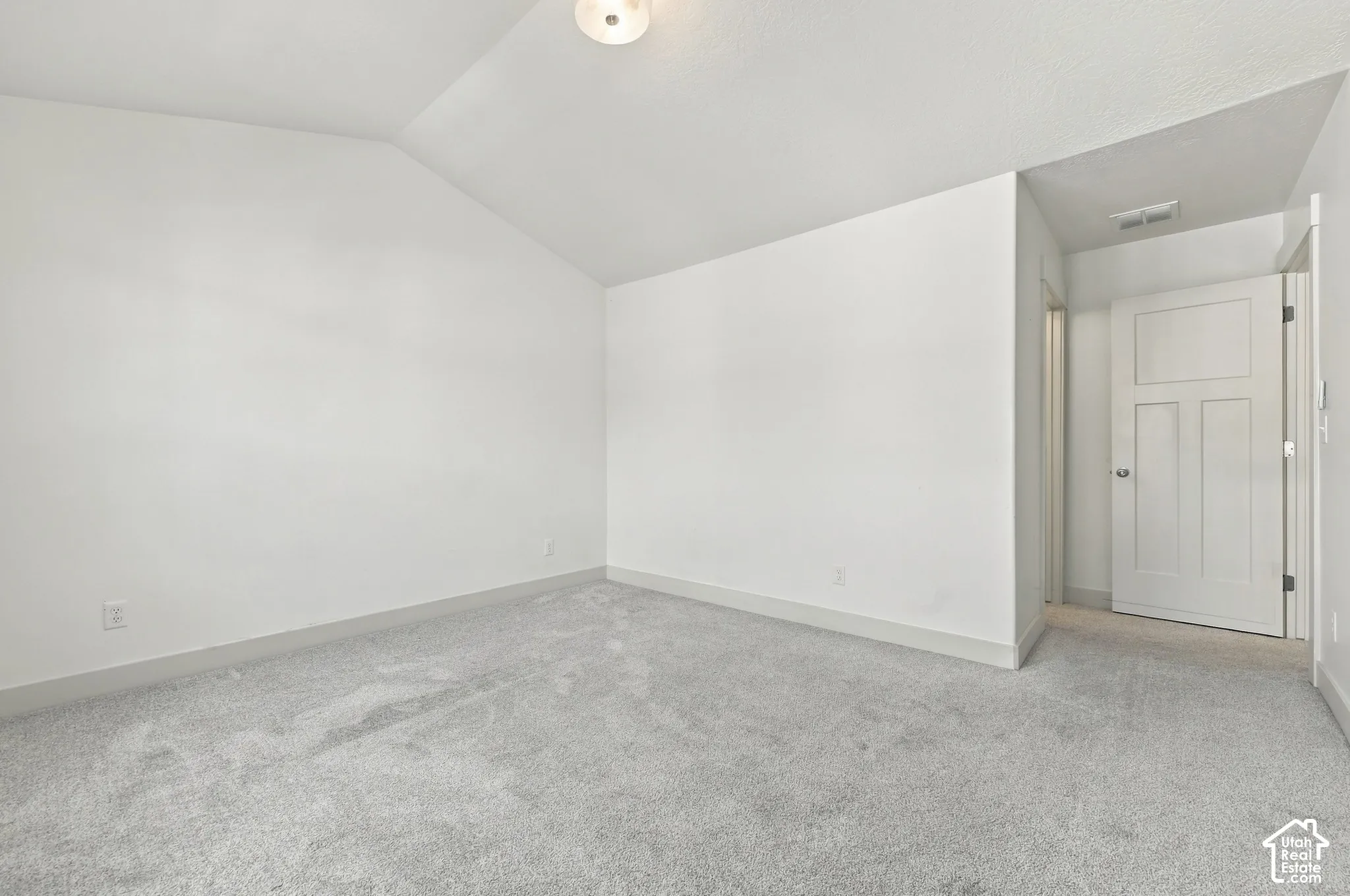 Vaulted ceiling room with light gray carpeting and a three-panel interior door