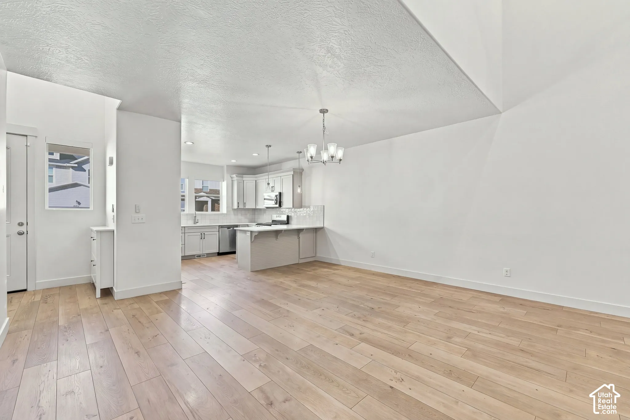Open-concept layout with wood-finish flooring, white walls, and a contemporary light fixture