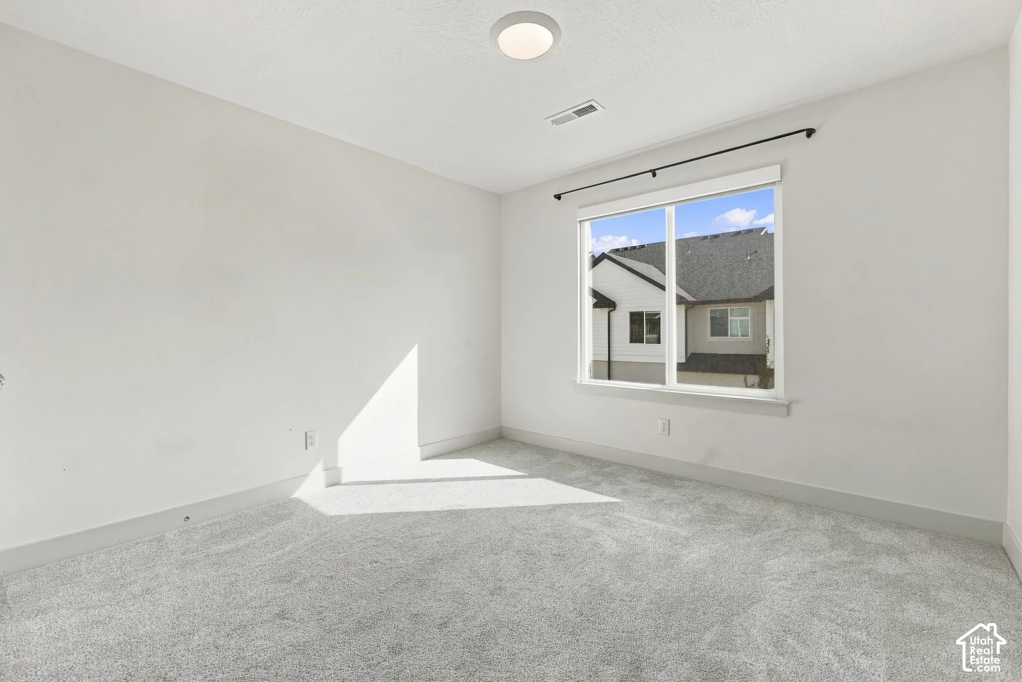 Recessed lighting, large window with black curtain rod, light gray carpeting, white walls, and white trim