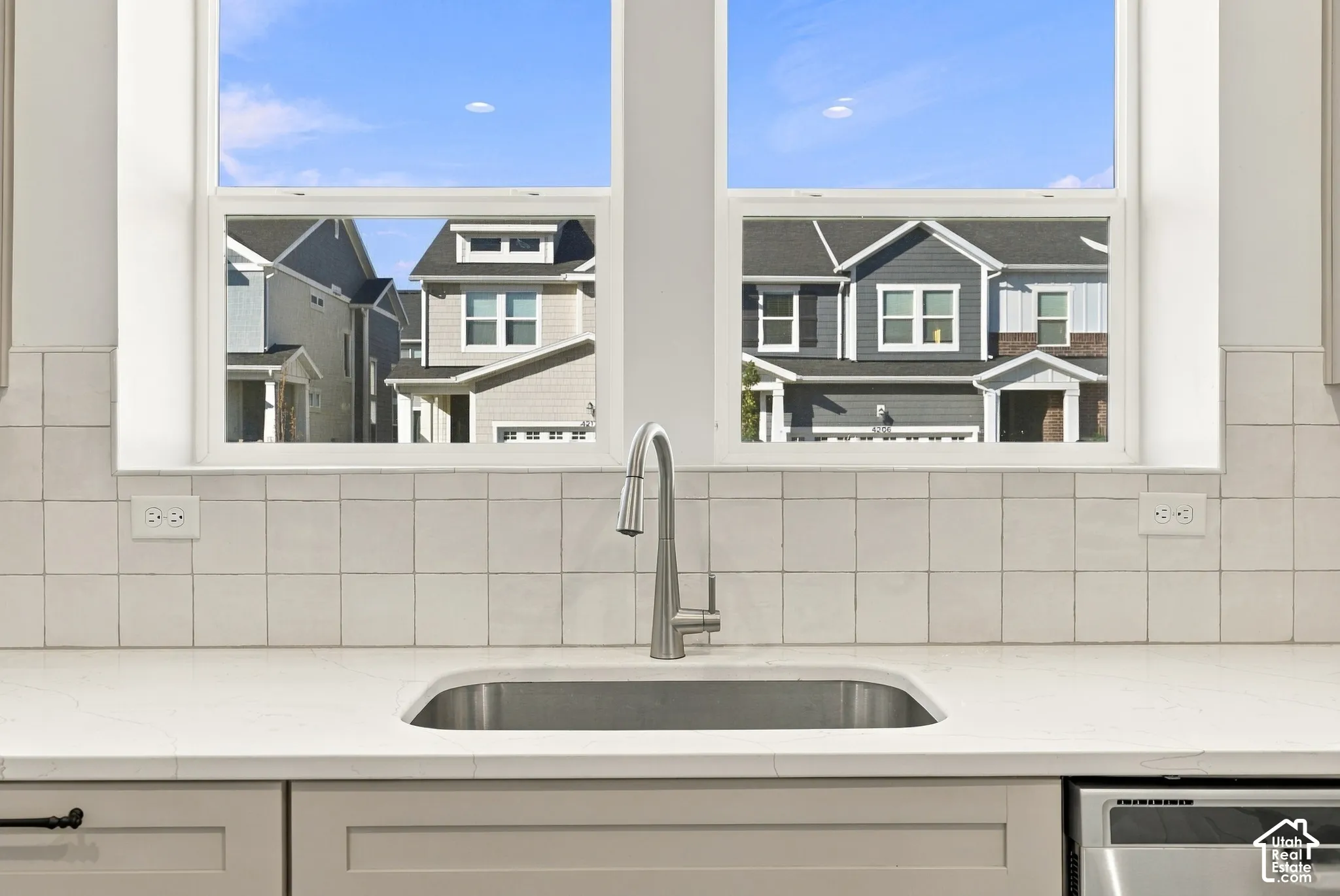 Stainless steel single-basin sink with a gooseneck faucet, light-toned countertop, and light-toned tile backsplash