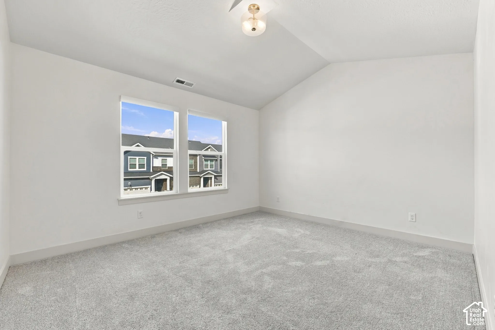 Vaulted ceiling with an attached light fixture, two windows with white trim, and light gray wall-to-wall carpeting