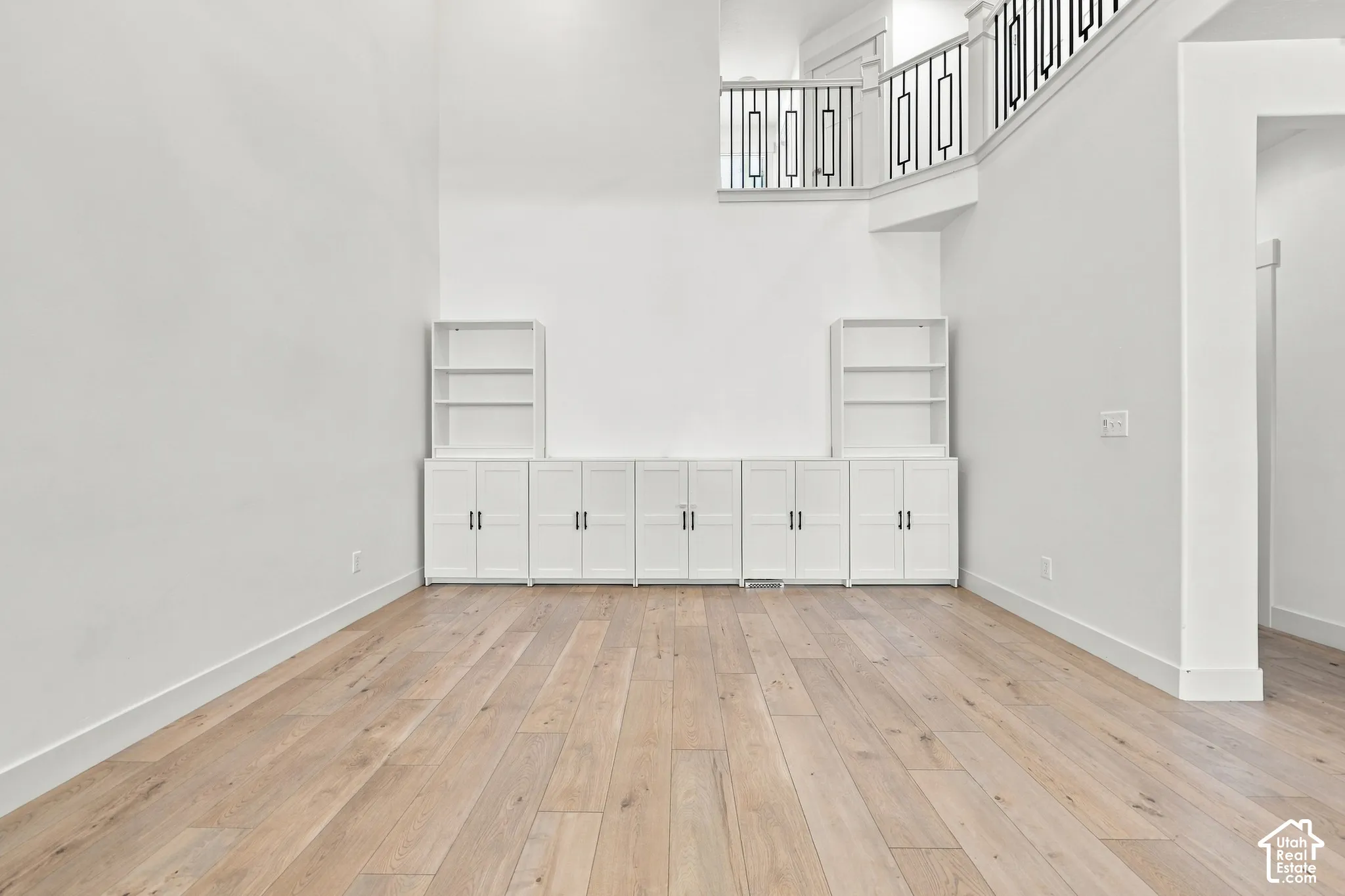 High ceilings, light wood-finish flooring, white built-in cabinetry, and a black wrought iron staircase railing