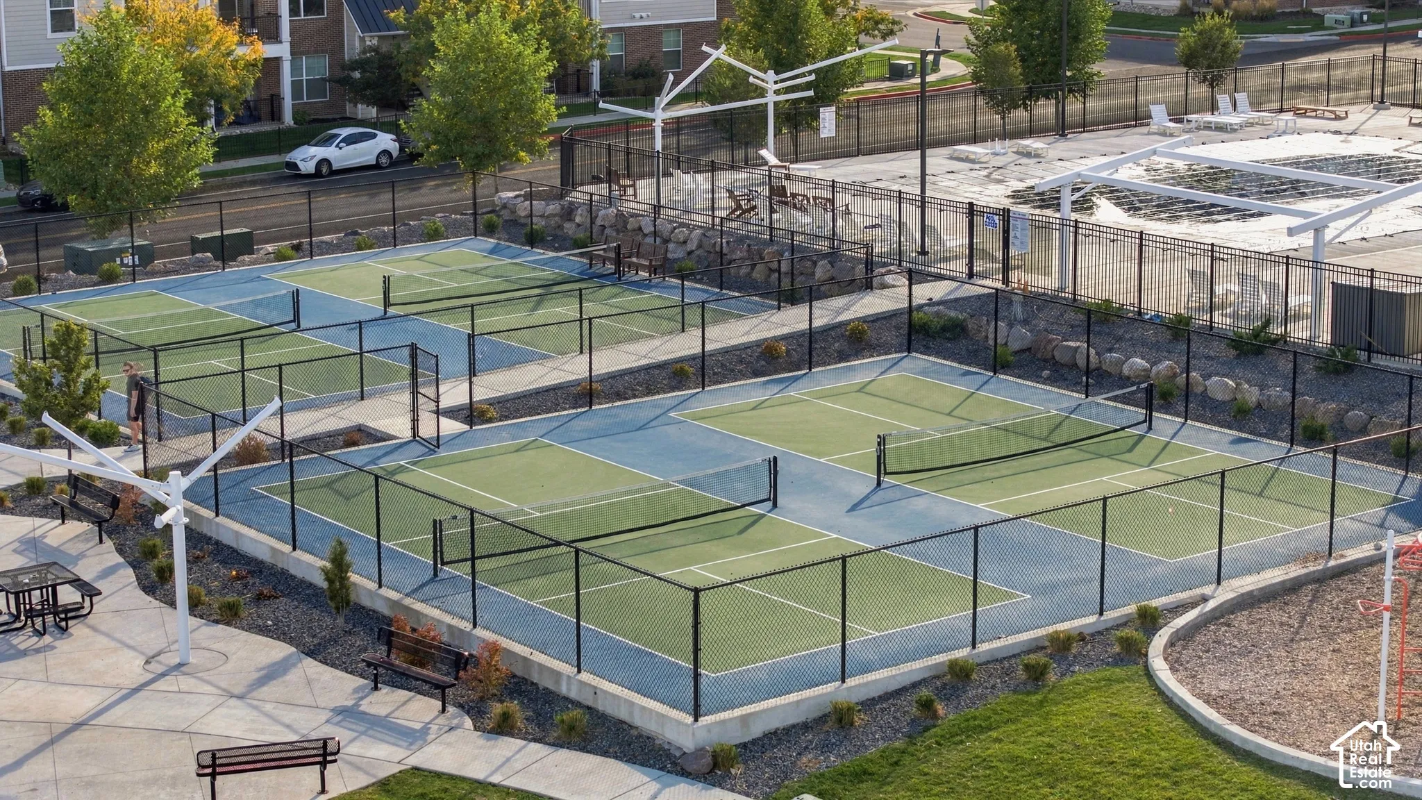 Multiple fenced pickleball courts, paved recreation area, picnic tables, and seating benches