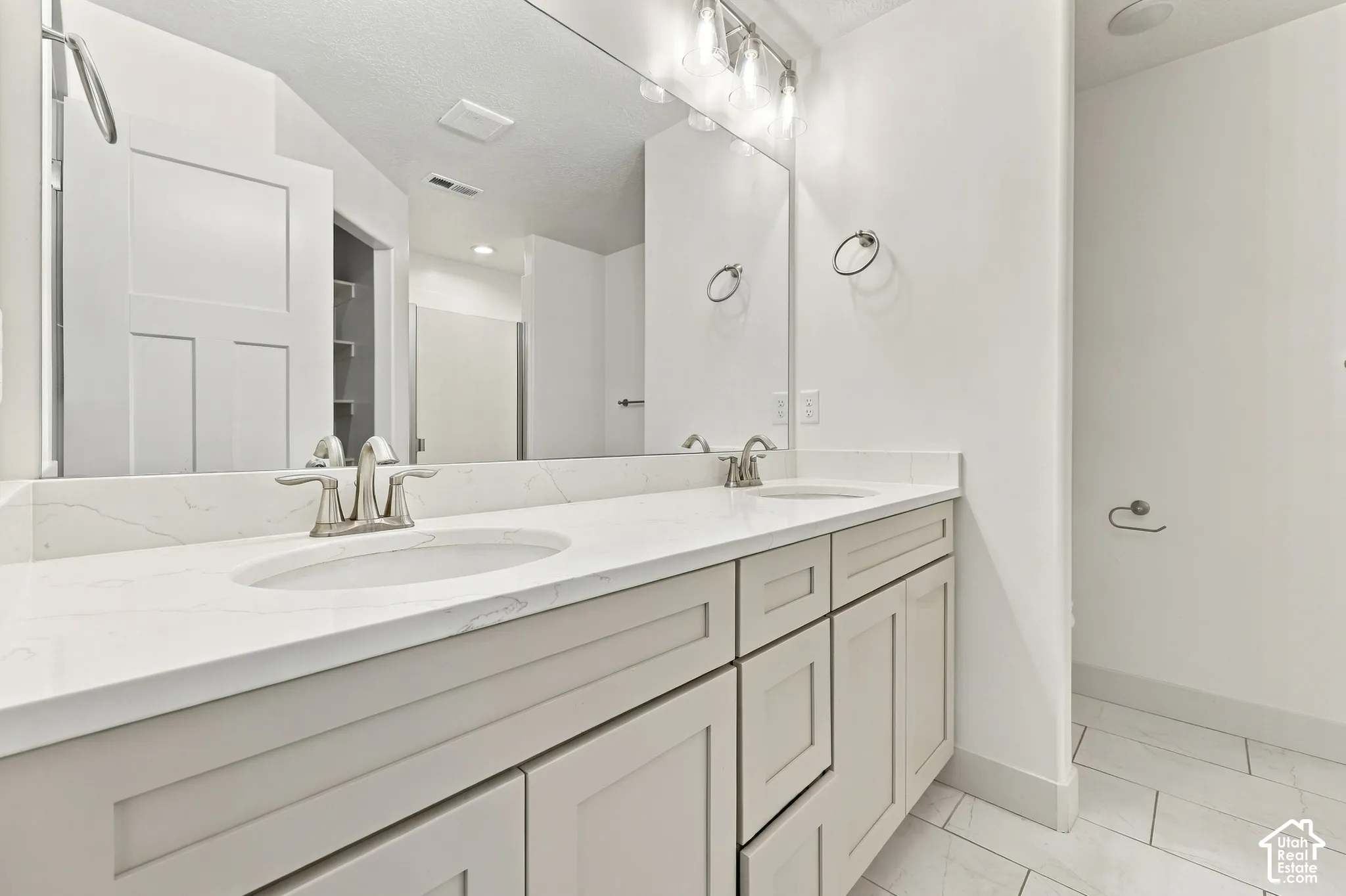 Dual vanity with undermount sinks and brushed nickel faucets, white countertop, large wall-mounted mirror, and tiled flooring