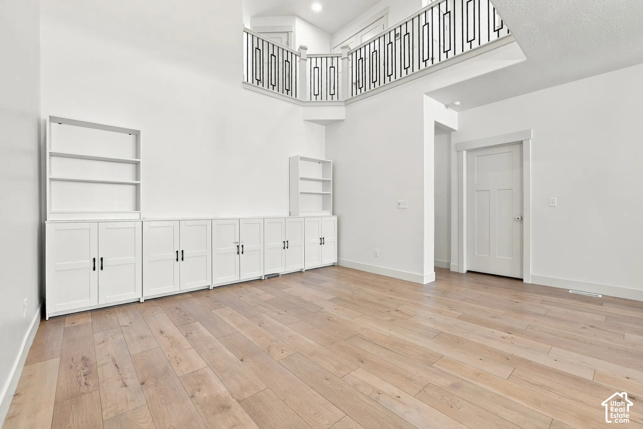 Expansive room featuring wood-finish flooring, white built-in cabinetry with open shelving, and a second-story interior balcony with an ornate railing