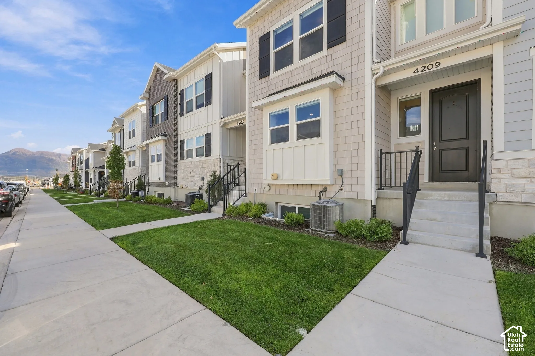 Modern multi-story facade featuring light-toned shake siding, contrasting dark shutters, a dark paneled entry door, a prominent street number, and a manicured lawn