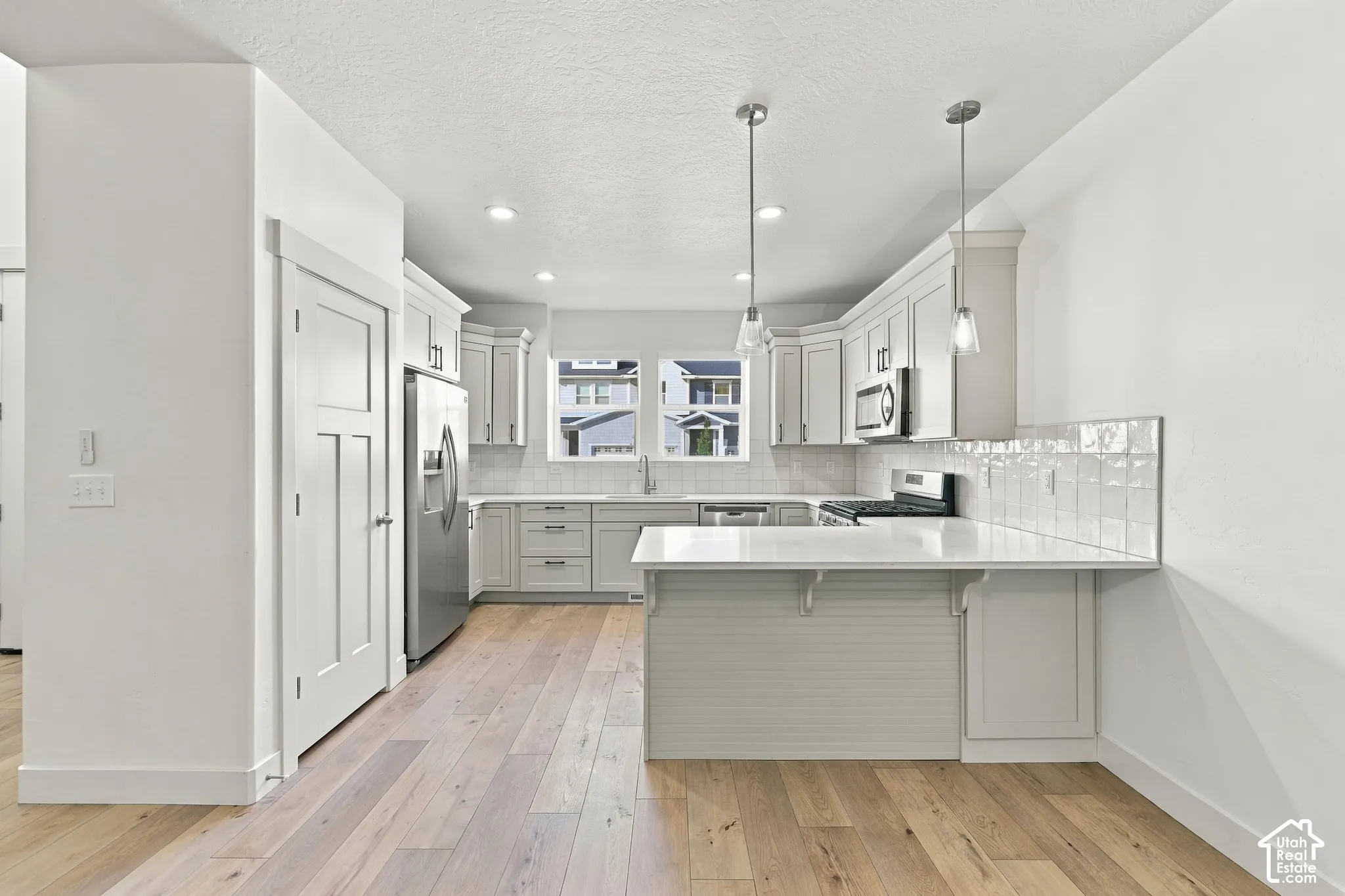 Kitchen featuring light wood-finish flooring, white cabinetry, integrated stainless steel appliances, a white tile backsplash, and pendant lighting