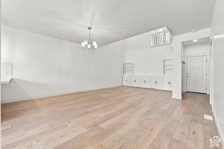 Expansive living space featuring wood-finish flooring, a contemporary chandelier, built-in cabinetry with open shelving, and a prominent front entry door