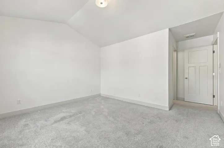 Vaulted ceiling room with light gray carpeting and a three-panel interior door
