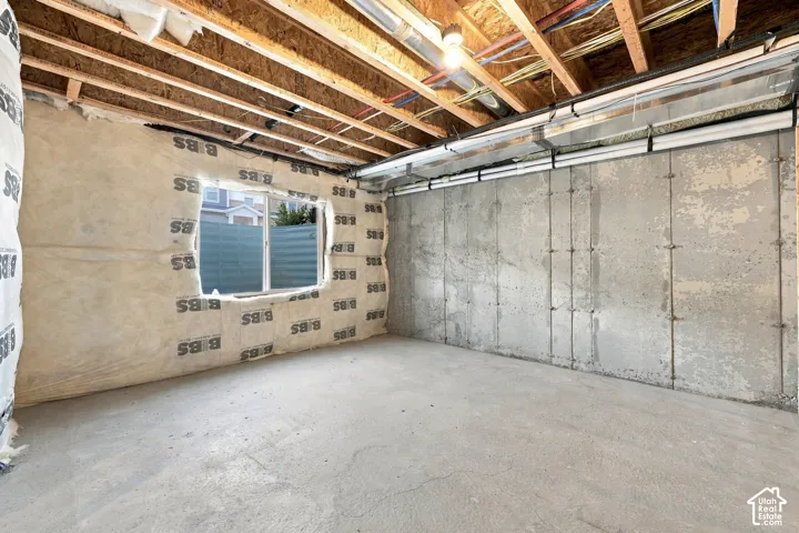Unfinished basement space featuring exposed wood joists, concrete flooring, and a single window