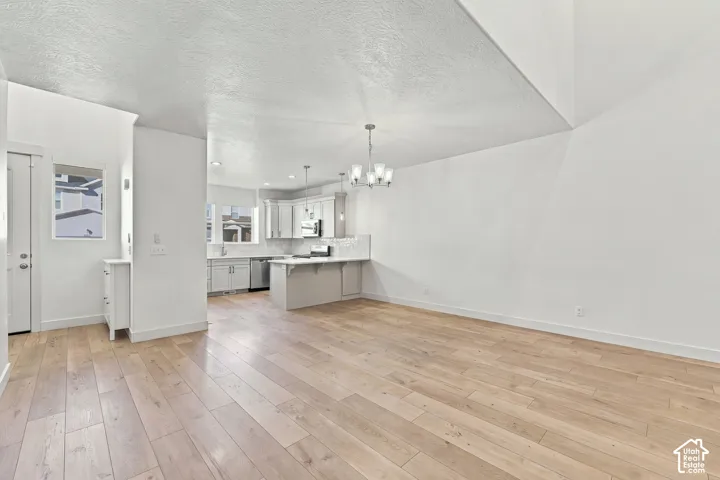 Open-concept layout with wood-finish flooring, white walls, and a contemporary light fixture