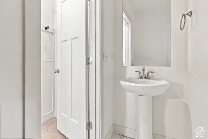 Pedestal sink with a chrome faucet, wall-mounted mirror, and wood-finish flooring