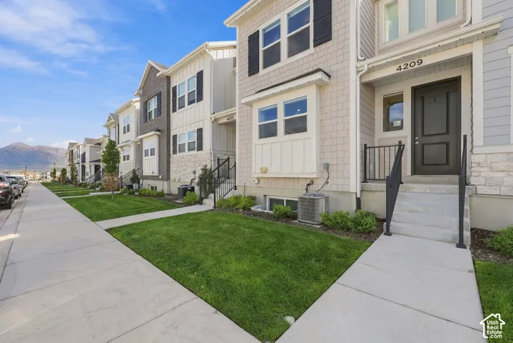 Modern multi-story facade featuring light-toned shake siding, contrasting dark shutters, a dark paneled entry door, a prominent street number, and a manicured lawn
