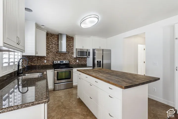Kitchen featuring a wood-finish island countertop, white cabinetry, dark stone countertops, stainless steel appliances, and a tiled backsplash