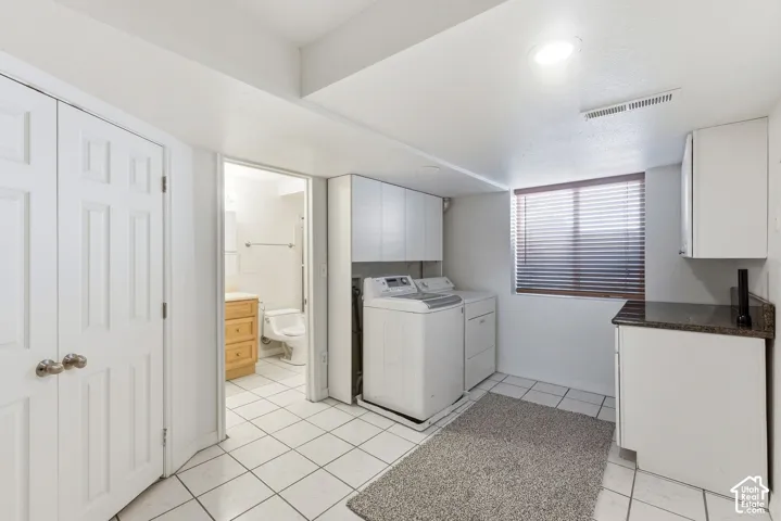 White tile flooring, white cabinetry, dark stone countertop, built-in recessed lighting, and a window with blinds