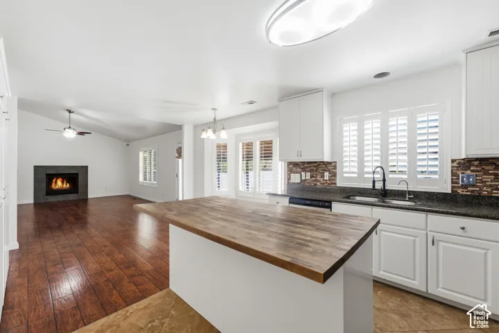 Kitchen island with wood-finish countertop, white cabinetry with dark hardware, dark countertops, tile backsplash, and a stainless steel sink with a matte black faucet