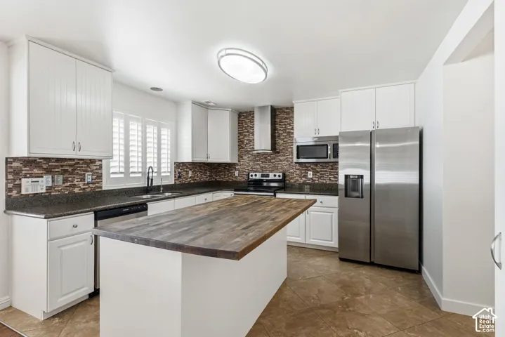 Kitchen featuring white cabinetry, dark countertops, a tiled backsplash, a central island with a wood-finish top, and stainless steel appliances