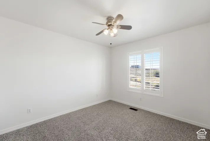 Window with plantation shutters, overhead lighting with ceiling fan, and grey carpeting