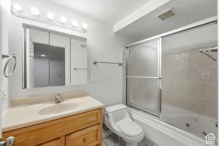 Light wood-finish vanity with an integrated sink, tri-fold mirrored medicine cabinet, and a bathtub with a tiled surround