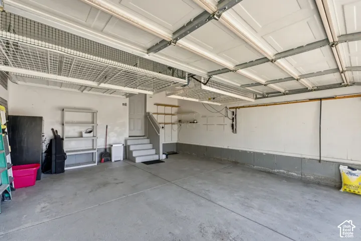Finished garage with concrete flooring, overhead storage racks, interior access door, and built-in shelving