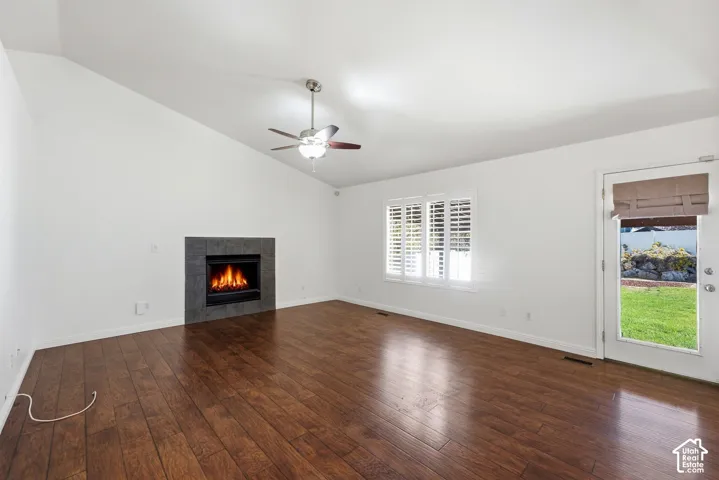 Vaulted ceiling with a ceiling fan, a fireplace with a dark tiled surround, wood-finish flooring, a window with white louvered shutters, and a glass-paneled door