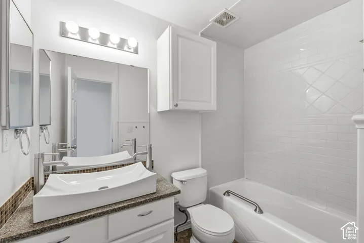 White ceramic vessel sink, granite-style countertop, white subway tile shower surround with decorative accent, and a built-in grab bar