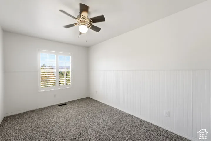 Plush carpeting, window with plantation shutters, ceiling fan with integrated lighting, and wainscoting