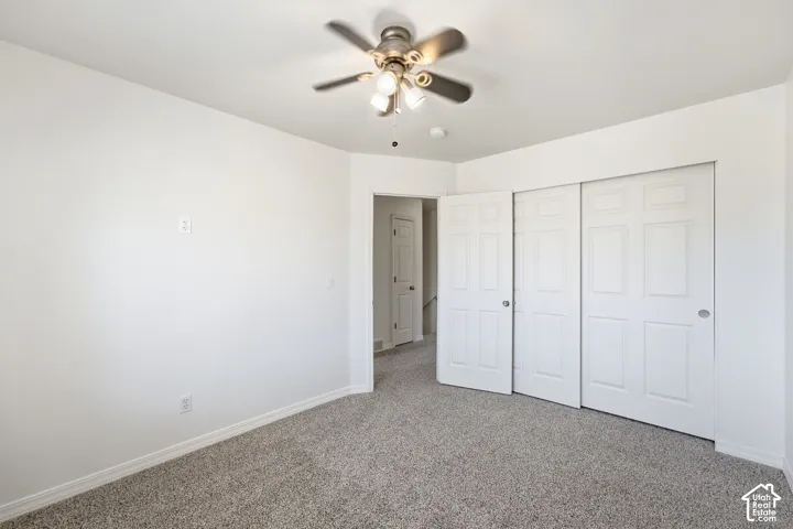 Textured carpeting, white walls, ceiling fan with integrated lighting, and sliding panel closet doors