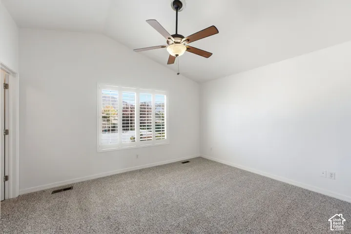 Vaulted ceiling with a ceiling fan, carpeted flooring, and window with plantation shutters