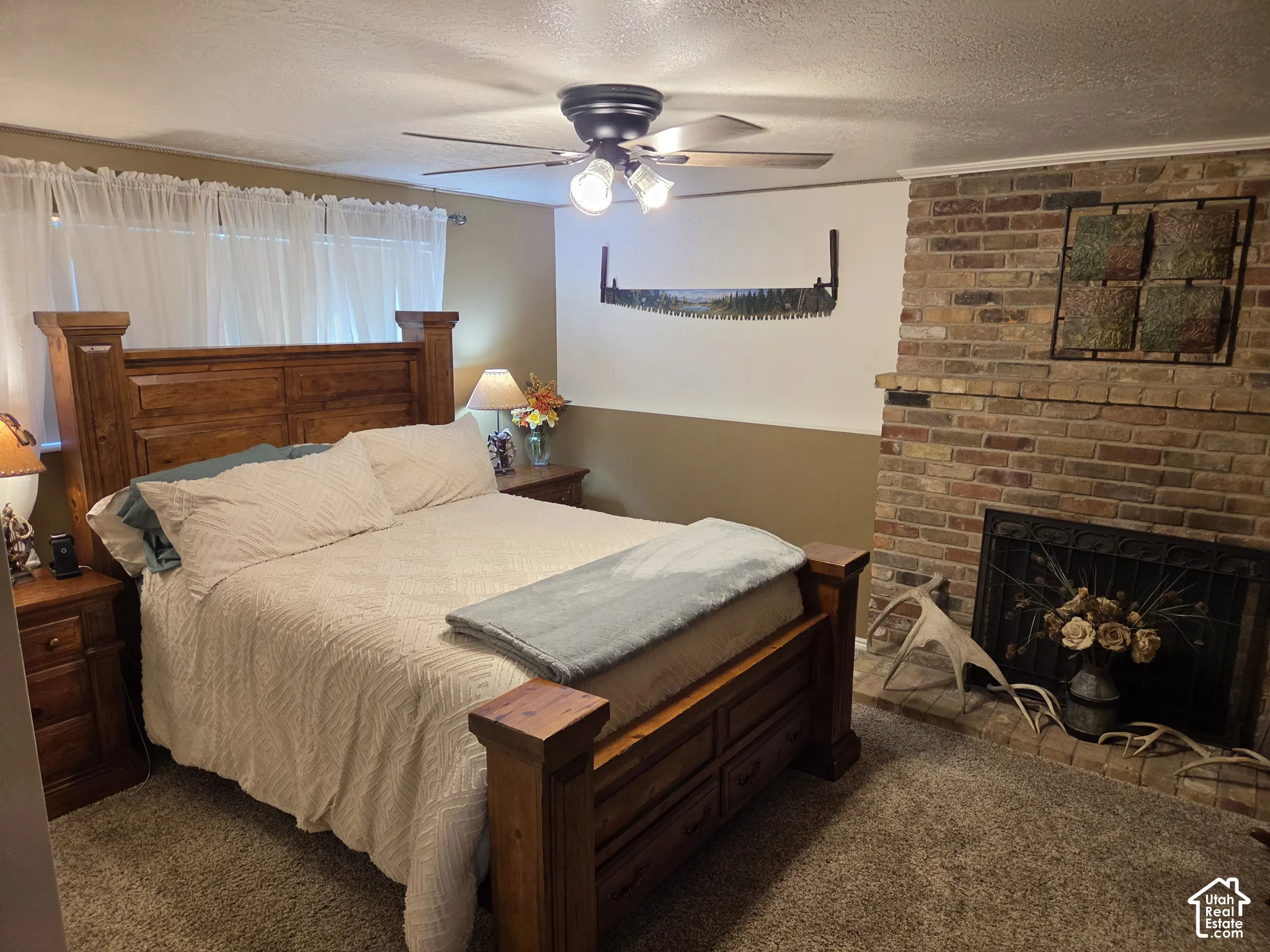 Brick fireplace with a metal screen, overhead ceiling fan with lighting, and wall-to-wall carpeting