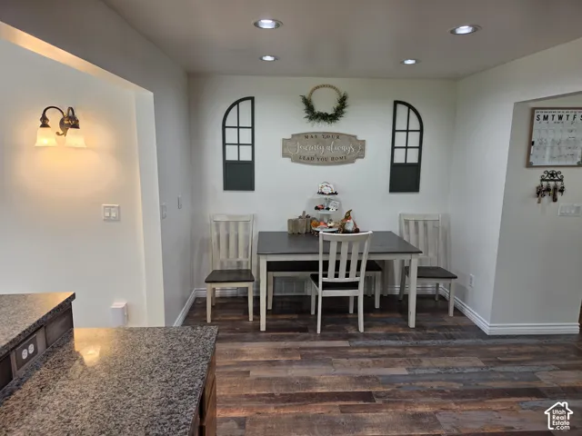 Recessed ceiling lighting, wood-finish flooring, white baseboards, and a built-in kitchen counter with a stone finish