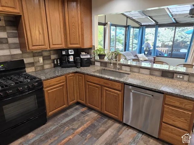 Kitchen featuring wood-finish cabinetry, granite-style countertops, a stainless steel sink with a gooseneck faucet, a black gas range, and a stainless steel dishwasher