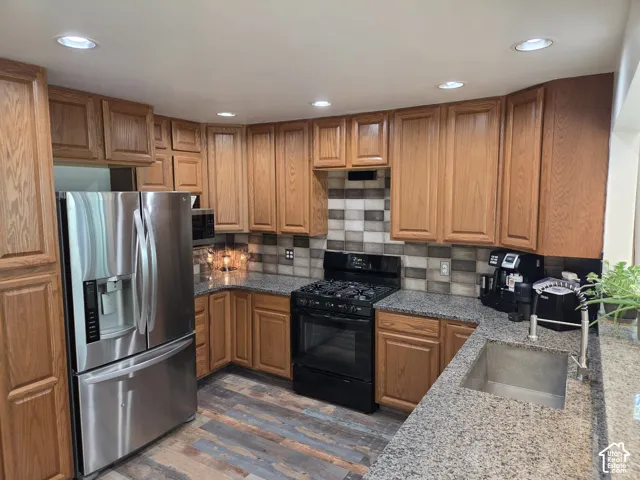 Kitchen featuring wood cabinetry, stainless steel refrigerator, granite countertops, tile backsplash, and wood-finish flooring