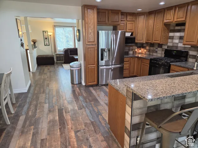 Kitchen featuring wood-finish flooring, wood cabinetry, stainless steel appliances, granite countertops, and a tiled backsplash