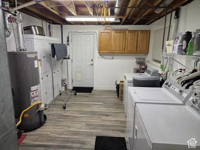 Wood-finish flooring, white built-in cabinetry, additional wood cabinetry, washer and dryer appliances, and a water heater
