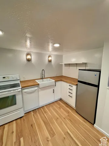 White shaker-style cabinetry with matte black hardware, wood-finish countertops, apron-front sink with a gooseneck faucet, and light wood-finish flooring