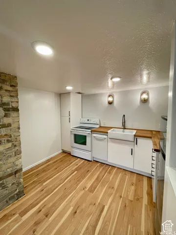 Wood-finish flooring, white cabinetry with black hardware, farmhouse sink, wood countertops, and modern ceiling lighting