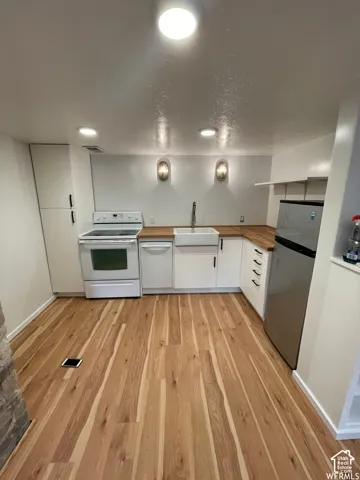 White shaker cabinetry with black hardware, wood-finish flooring, undermount sink, recessed ceiling lighting, and wall-mounted sconces