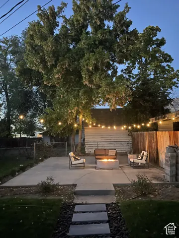 Concrete patio with string lighting, a stone fire pit, and a fenced perimeter