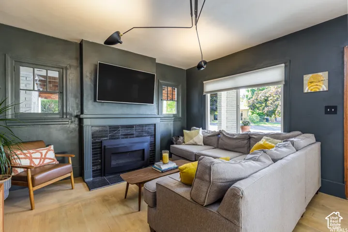 Hardwood-style flooring, fireplace with dark tile surround, mantel, large window, and dark accent walls