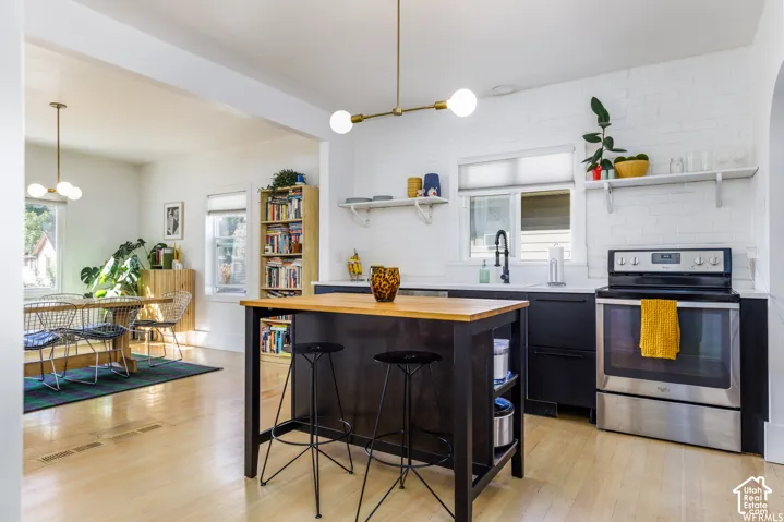 Kitchen featuring light wood-finish flooring, white brick-patterned walls, dark cabinetry, and a central island with a wood-finish countertop