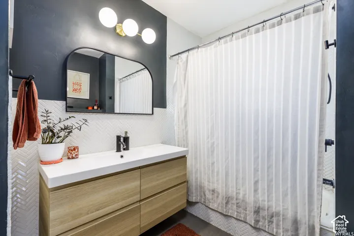 Floating wood-finish vanity with an integrated sink and matte black faucet, herringbone tile wainscoting, and a curved arch-top mirror