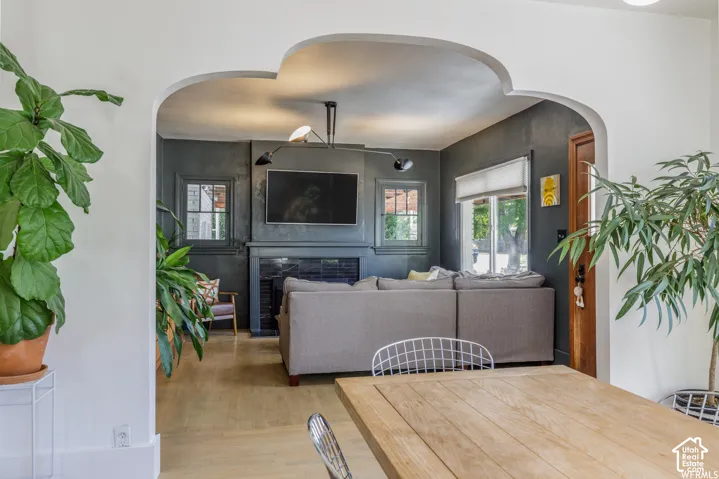 Arched entryway framing a living space with wood-finish flooring, a fireplace with a dark mantel, and multiple windows