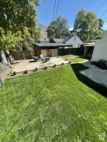Expansive lawn area with a concrete patio, wood fencing, and mature trees