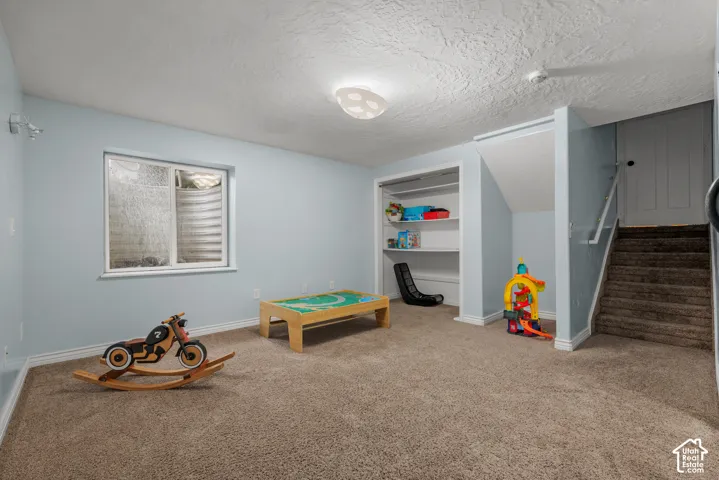 Carpeted room featuring a single window, built-in shelving, a recessed area under the stairs, and a staircase with a handrail