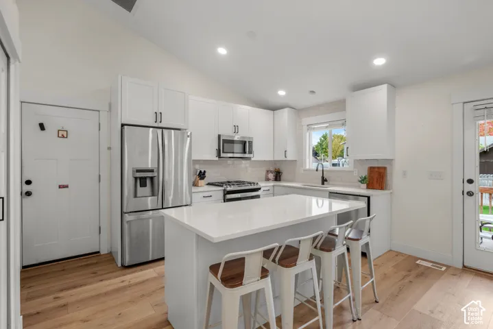 Modern kitchen featuring stainless steel appliances, white cabinetry, a center island with countertop seating, and light wood-finish flooring