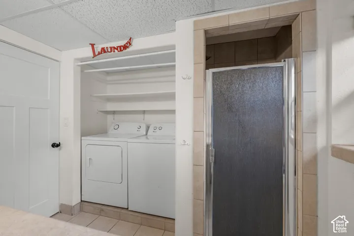 Laundry area with shelving, washer and dryer units, and a glass-enclosed shower with tiled surround